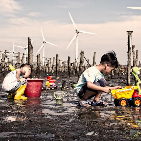 kids playing in the mud in front of wind turbines