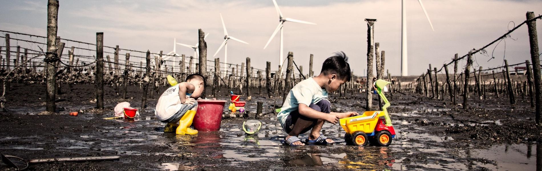 kids playing in the mud in front of wind turbines